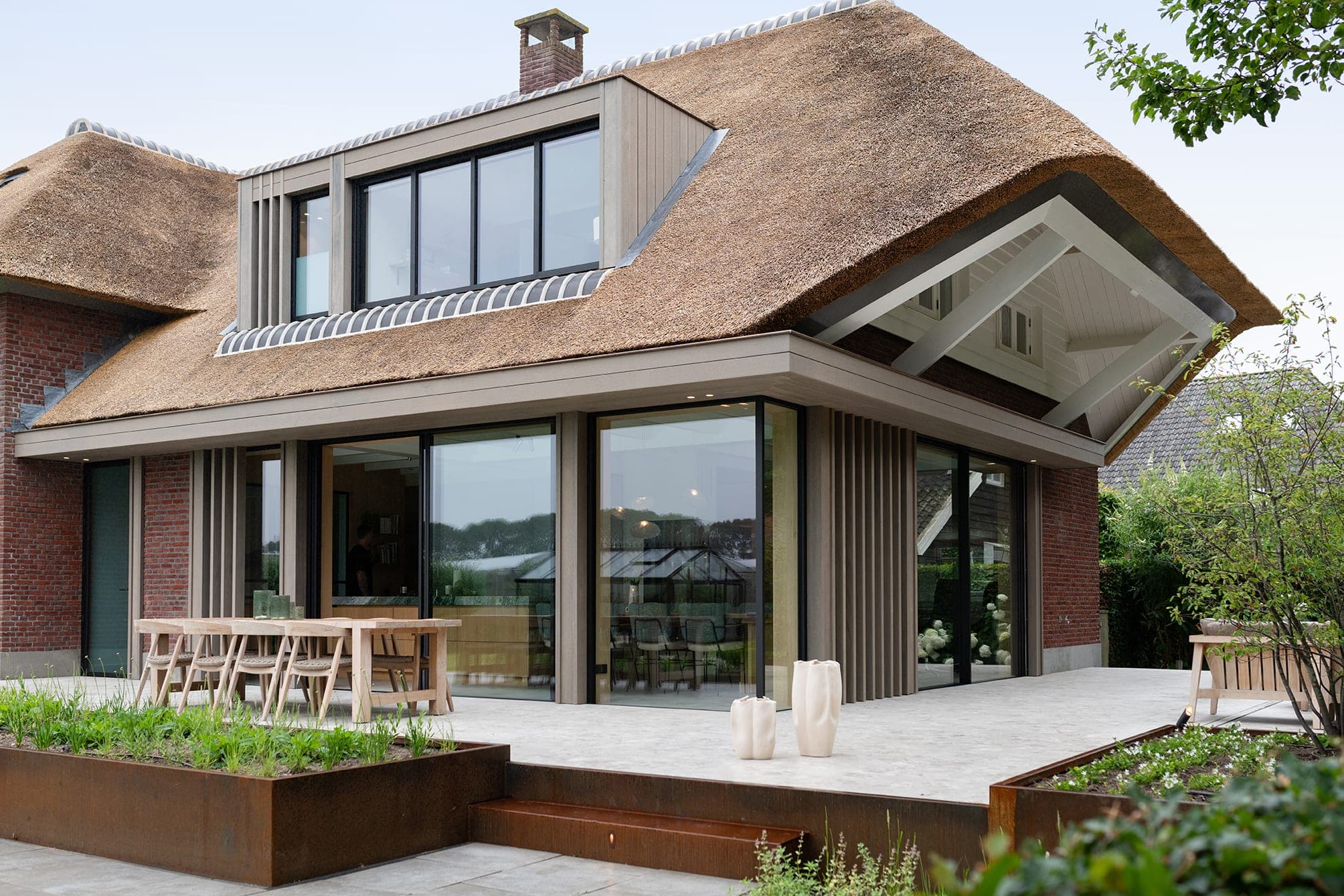De nieuwe uitbouw onder de rieten kap, met terras en cortenstalen plantenbakken